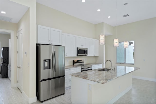 kitchen with light stone countertops, appliances with stainless steel finishes, pendant lighting, white cabinetry, and an island with sink