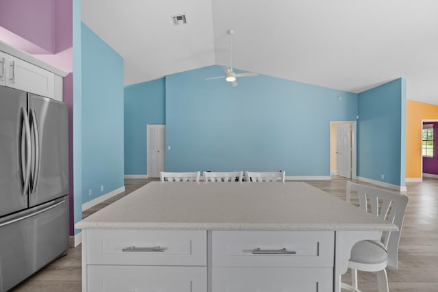 kitchen with stainless steel refrigerator, a breakfast bar, a kitchen island, and white cabinets