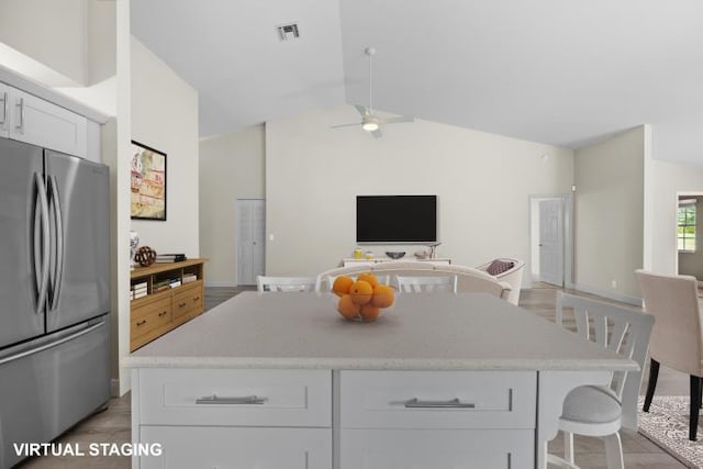 kitchen featuring lofted ceiling, a breakfast bar, a center island, stainless steel refrigerator, and white cabinets