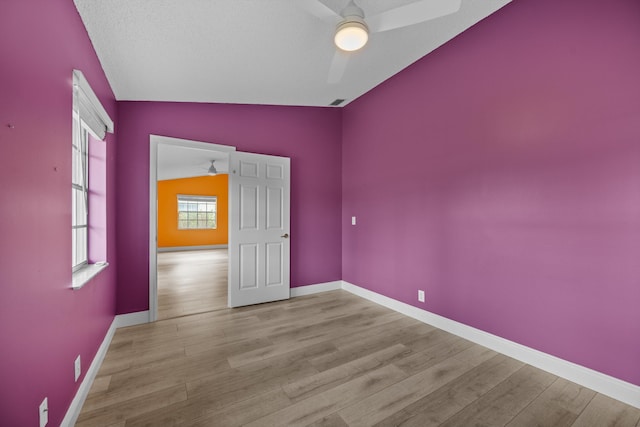 spare room with ceiling fan, lofted ceiling, a textured ceiling, and light hardwood / wood-style floors