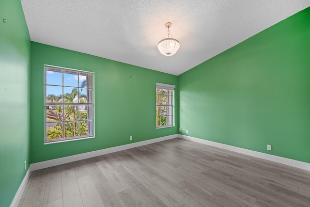 spare room featuring an inviting chandelier, light hardwood / wood-style floors, and a textured ceiling