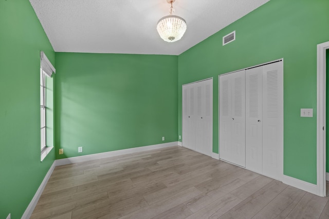 unfurnished bedroom with multiple closets, a textured ceiling, a chandelier, and light wood-type flooring