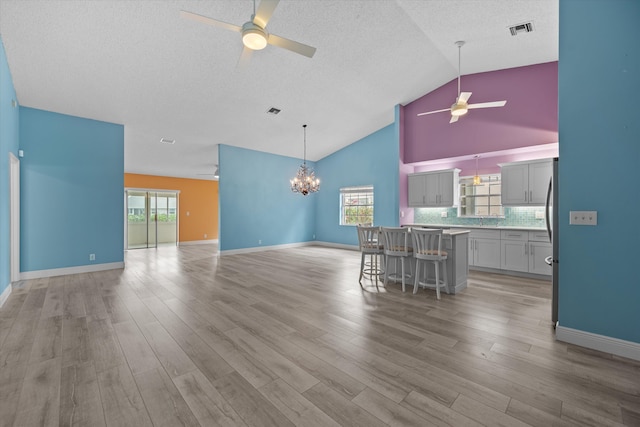 interior space featuring a breakfast bar, gray cabinetry, tasteful backsplash, a kitchen island, and ceiling fan with notable chandelier