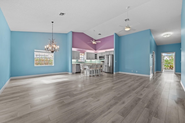 unfurnished living room with vaulted ceiling, a healthy amount of sunlight, ceiling fan with notable chandelier, and light wood-type flooring