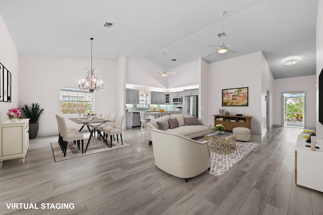 living room with high vaulted ceiling, ceiling fan with notable chandelier, light hardwood / wood-style flooring, and a textured ceiling