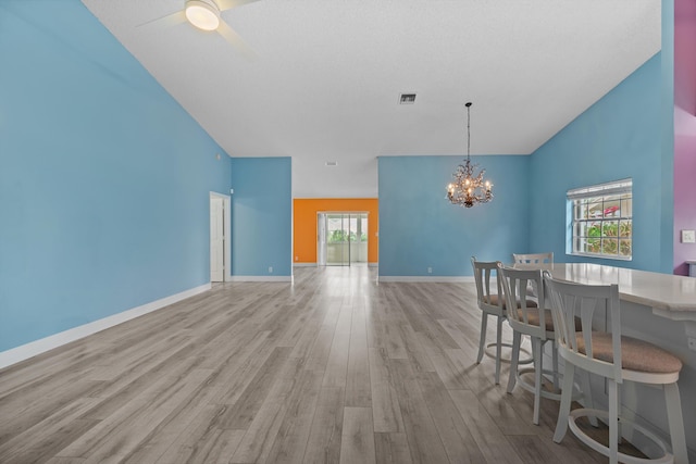 unfurnished dining area featuring ceiling fan with notable chandelier and light wood-type flooring