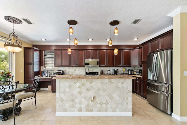 kitchen with appliances with stainless steel finishes, a kitchen island with sink, crown molding, light tile patterned floors, and hanging light fixtures