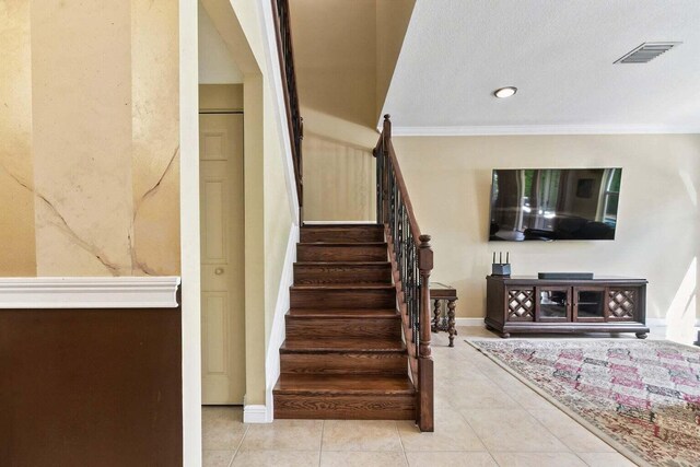 staircase featuring tile patterned flooring, a textured ceiling, and ornamental molding