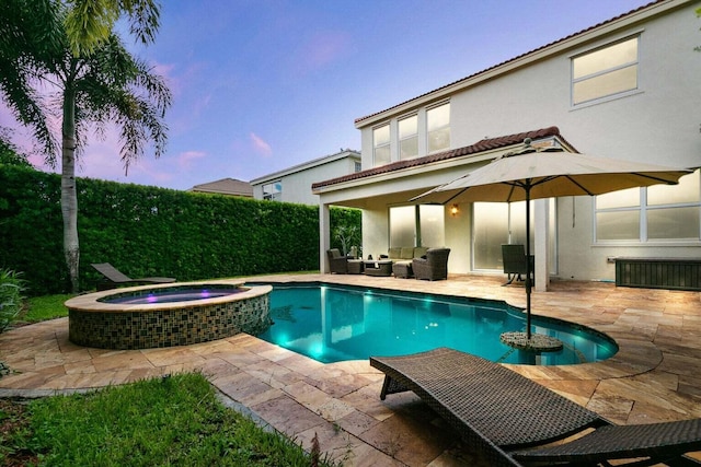 pool at dusk with an in ground hot tub, outdoor lounge area, and a patio area