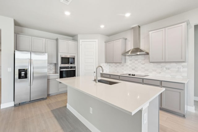 kitchen with wall chimney range hood, sink, a center island with sink, and black appliances