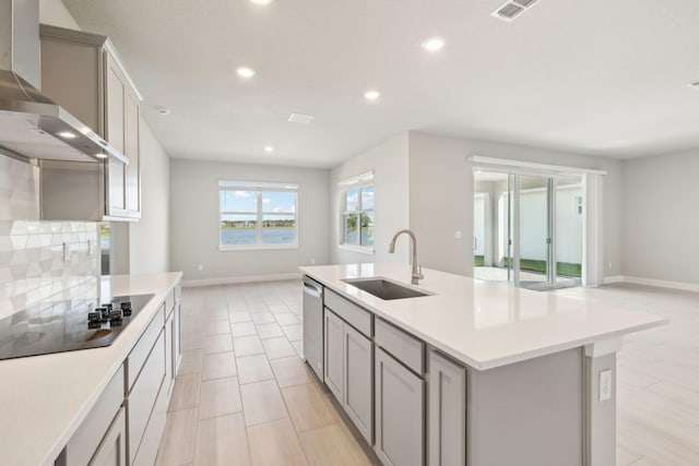 kitchen with gray cabinets, sink, a kitchen island with sink, and wall chimney exhaust hood