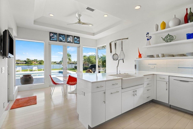 kitchen featuring dishwasher, a tray ceiling, white cabinets, ceiling fan, and sink