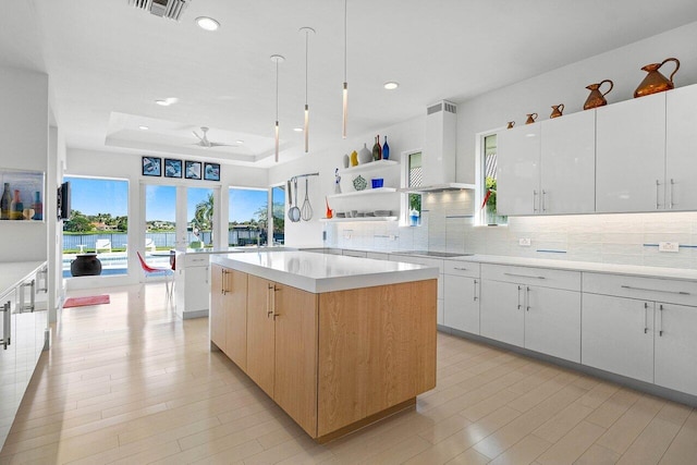 kitchen featuring white cabinets, a center island, a raised ceiling, ceiling fan, and black electric stovetop