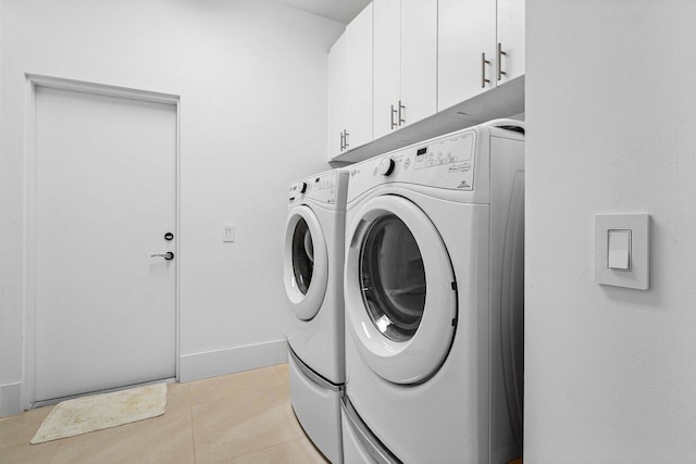 clothes washing area featuring cabinets, washing machine and clothes dryer, and light tile patterned floors