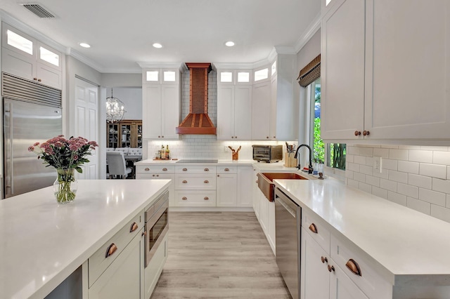 kitchen featuring custom range hood, built in appliances, white cabinetry, and sink