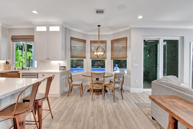 dining room with ornamental molding, light wood-type flooring, a notable chandelier, and sink