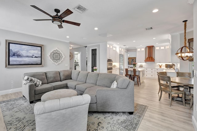 living room with light wood-type flooring, ceiling fan with notable chandelier, and crown molding