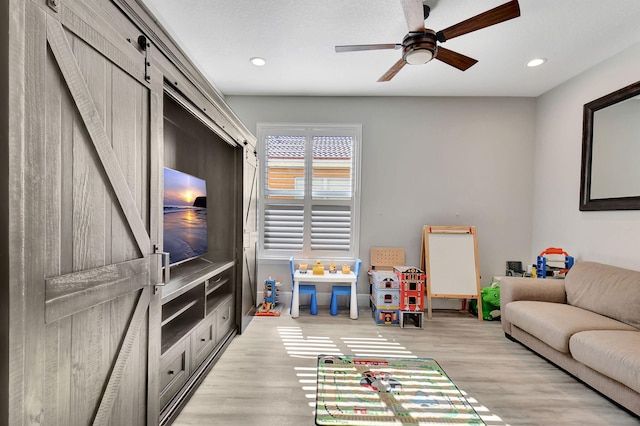 playroom with a barn door, light hardwood / wood-style floors, and ceiling fan