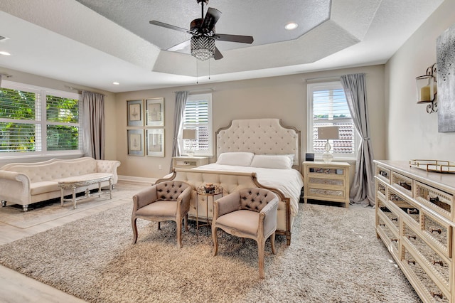 bedroom featuring a textured ceiling, a tray ceiling, and ceiling fan