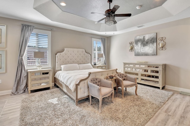 bedroom with hardwood / wood-style floors, ceiling fan, multiple windows, and a tray ceiling