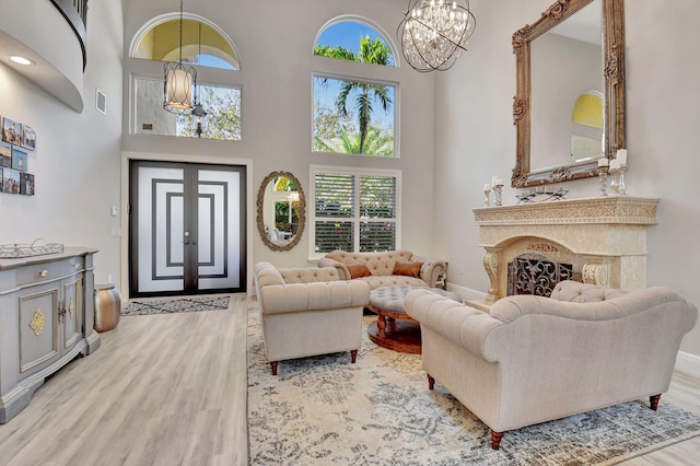 living room featuring a notable chandelier, light wood-type flooring, a fireplace, and a high ceiling