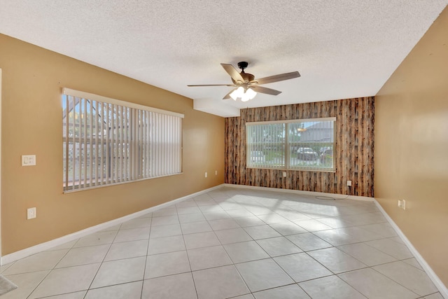 unfurnished room with light tile patterned floors, wood walls, a textured ceiling, ceiling fan, and baseboards