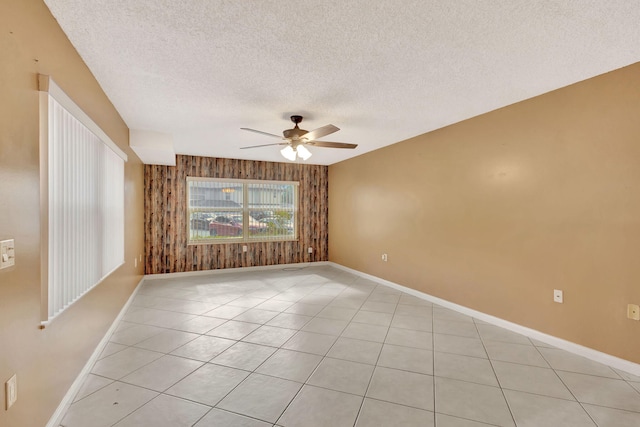 spare room featuring light tile patterned floors, wooden walls, baseboards, a ceiling fan, and a textured ceiling