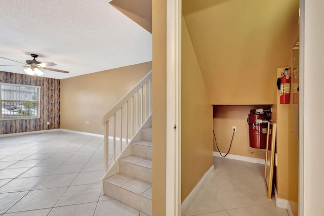 staircase with wooden walls, baseboards, ceiling fan, tile patterned flooring, and a textured ceiling