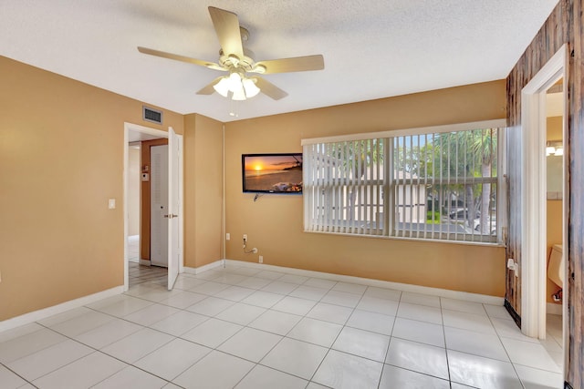 empty room with a textured ceiling, light tile patterned floors, visible vents, and baseboards