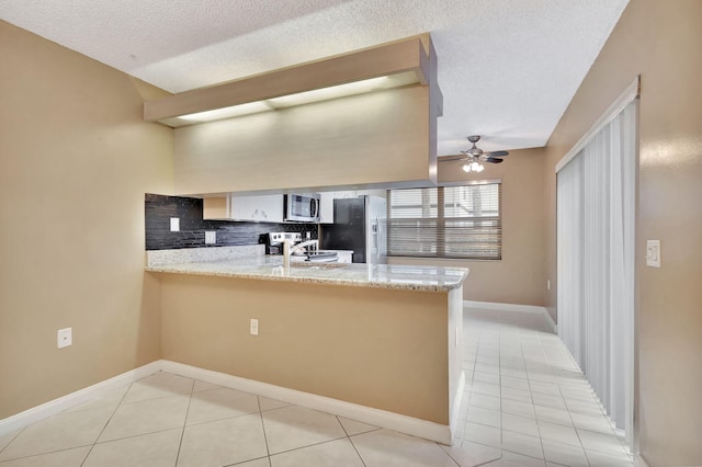 kitchen featuring tasteful backsplash, appliances with stainless steel finishes, ceiling fan, a sink, and a peninsula