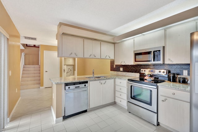 kitchen featuring light stone counters, a peninsula, a sink, appliances with stainless steel finishes, and backsplash