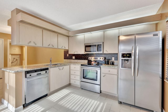 kitchen featuring a peninsula, a sink, appliances with stainless steel finishes, backsplash, and light stone countertops