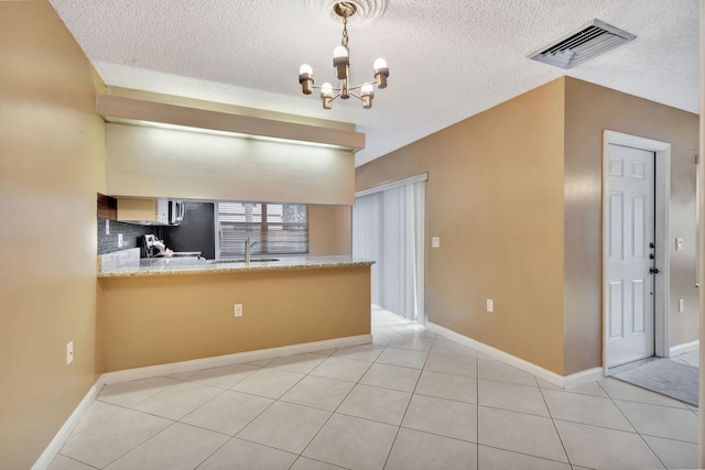 kitchen with light tile patterned floors, visible vents, a peninsula, an inviting chandelier, and pendant lighting