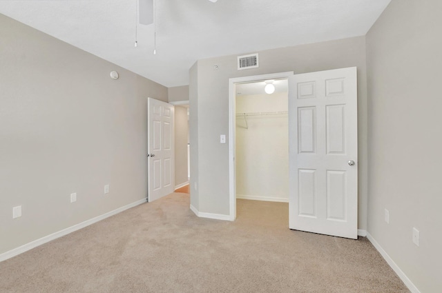 unfurnished bedroom featuring ceiling fan, a spacious closet, light carpet, and a closet