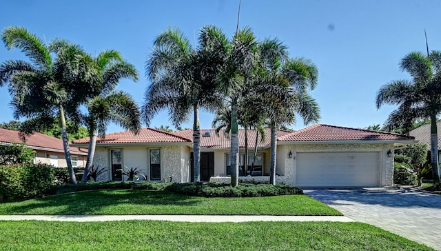 mediterranean / spanish-style home with stucco siding, a tile roof, decorative driveway, a front yard, and an attached garage