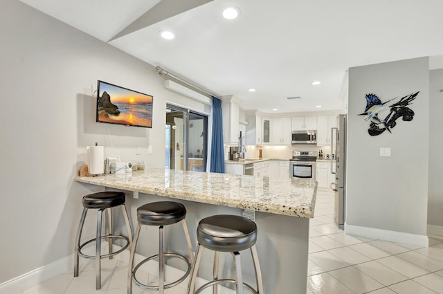 kitchen with white cabinetry, kitchen peninsula, lofted ceiling, a kitchen bar, and appliances with stainless steel finishes