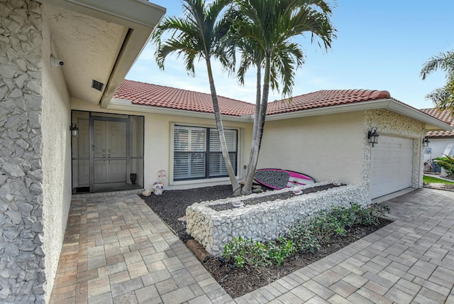 property entrance featuring stucco siding, an attached garage, and a tile roof