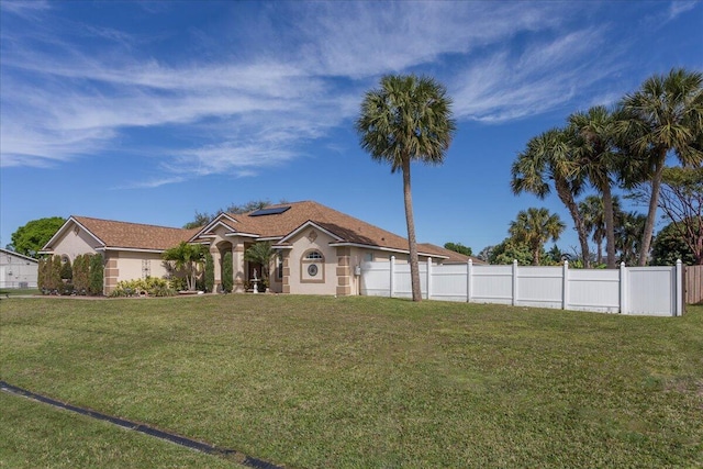 mediterranean / spanish-style home with roof mounted solar panels, a front lawn, and fence