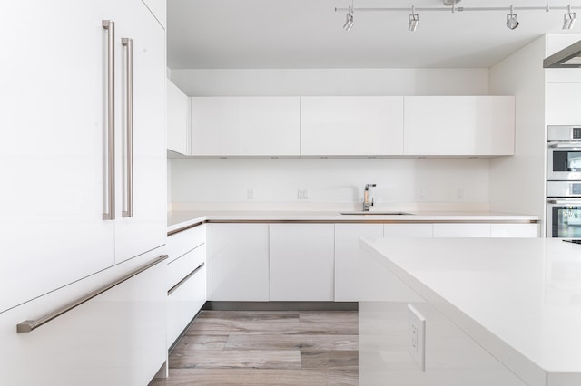 kitchen featuring track lighting, sink, double oven, high end fridge, and white cabinetry