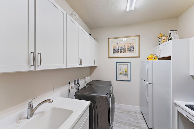 clothes washing area featuring washer and clothes dryer, sink, cabinets, and a textured ceiling