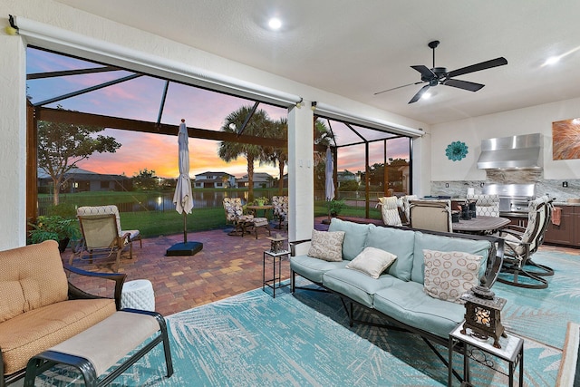 patio terrace at dusk with area for grilling, an outdoor living space, glass enclosure, and ceiling fan