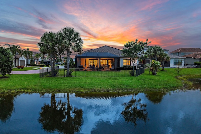 back house at dusk with a water view and a yard