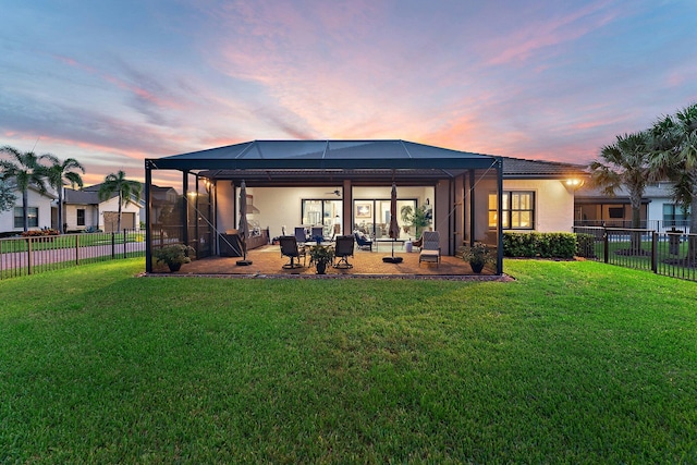 back house at dusk with a patio, a yard, and glass enclosure