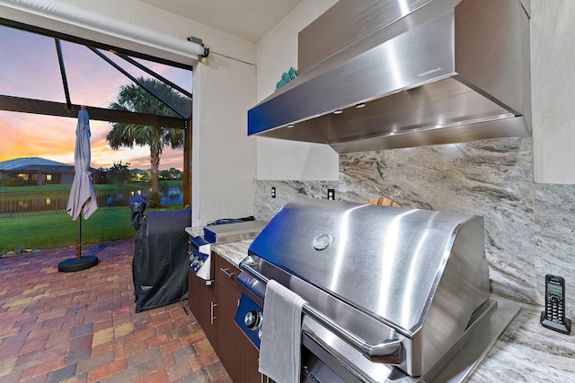 exterior space featuring dark brown cabinetry, wall chimney range hood, and light stone counters