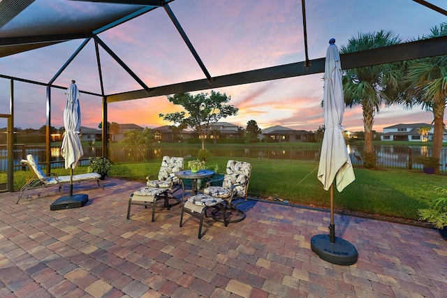 patio terrace at dusk with a yard, a water view, and glass enclosure