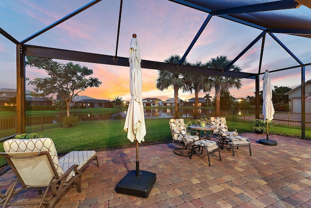 patio terrace at dusk with a water view, glass enclosure, and a lawn