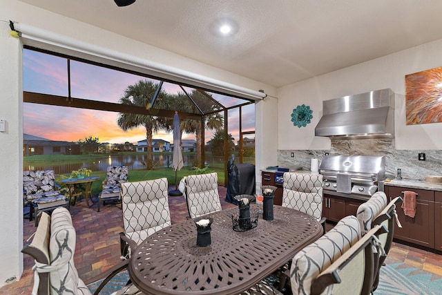 patio terrace at dusk featuring a water view, area for grilling, grilling area, and a lanai