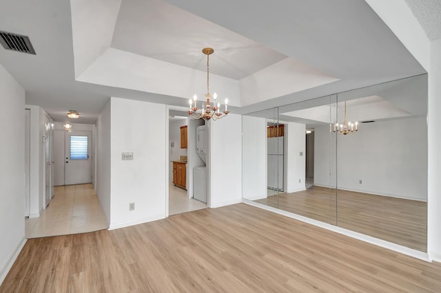 interior space with an inviting chandelier, light wood-type flooring, and a tray ceiling