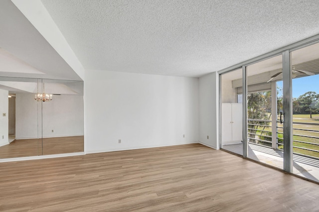 spare room with light wood-type flooring, an inviting chandelier, floor to ceiling windows, and plenty of natural light