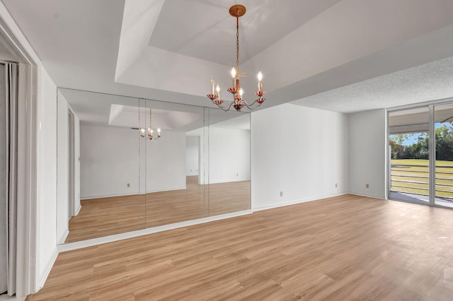 unfurnished living room featuring a raised ceiling, light wood-type flooring, and an inviting chandelier